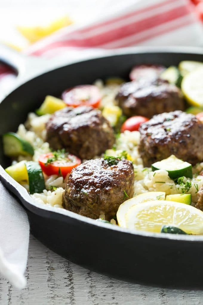 Una cazuela de albóndigas griegas con arroz al limón y tomates frescos.