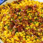 Maíz frito cubierto con tocino y cebollino en una sartén.