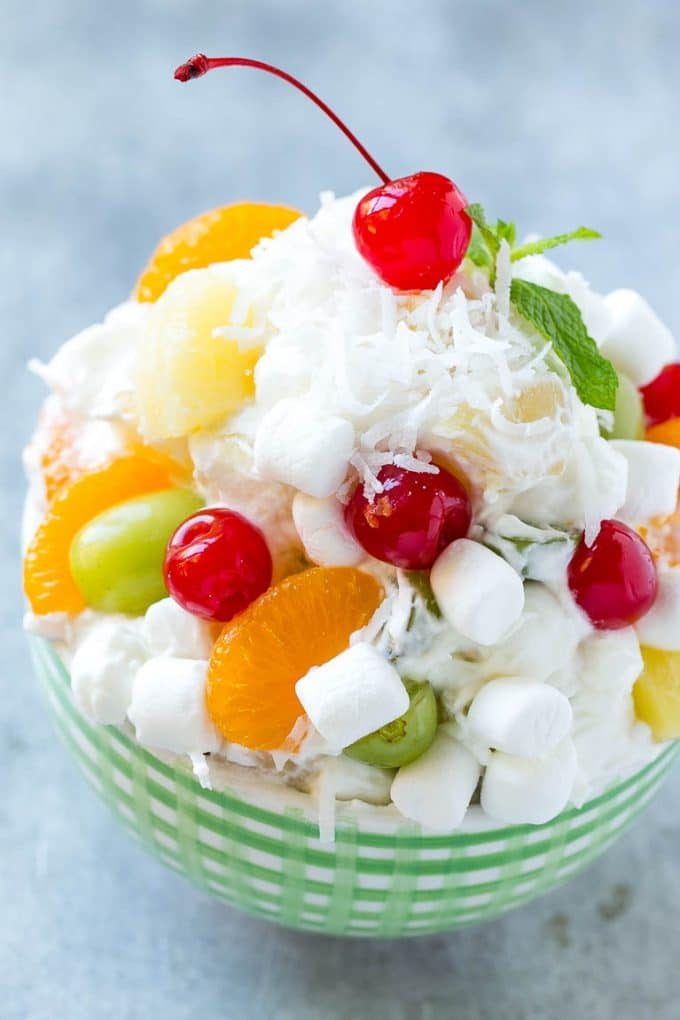 Un tazón de ensalada de ambrosía con una variedad de frutas coloridas con malvaviscos y coco, mezclado con un aderezo cremoso y ligero.
