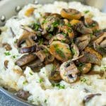 Una cacerola de risotto de champiñones cubierto con champiñones blanqueados y perejil.