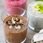 Tres tazas de pudín de chía bañadas en chocolate y frutas, luego rociadas con menta.