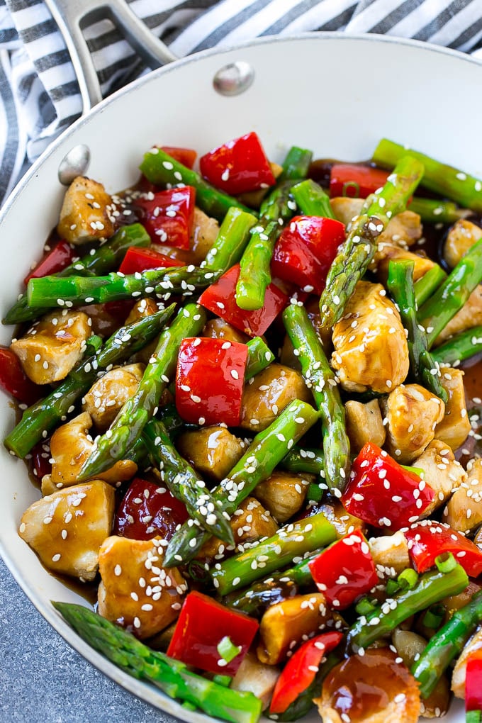 Una cacerola de pollo teriyaki salteado con trozos de pollo, espárragos y pimientos rojos.