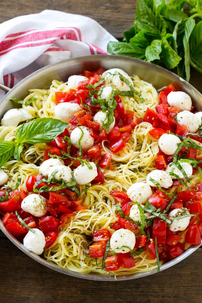 Una cacerola de pasta de cabello de ángel caprese cubierta con aceite de oliva, tomates, albahaca y mozzarella fresca.