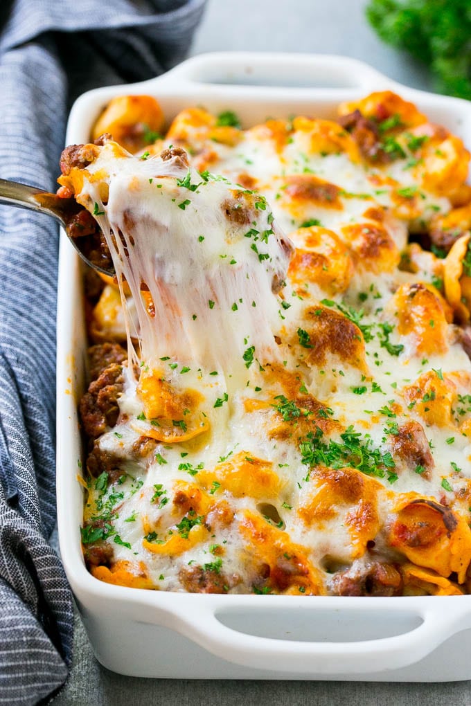 Receta Tortellini Al Forno Al Ragù | Tortellini con queso | Receta de Tortellini | Receta de pasta al horno #tortellini #tortellini al horno #salsa de carne #pasta #dinner #dinneratthezoo Una cazuela de queso y tortellini horneados con una cuchara levantando una porción.