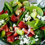 Un tazón de ensalada de fresas y espinacas con aderezo de semillas de amapola, queso feta y aguacate en rodajas.