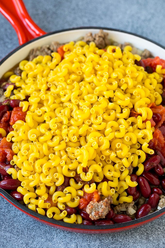 Macarrones crudos en una sartén con carne picada y tomates.