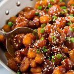 Una sartén de camarones crujientes con sésamo mezclados con una salsa al estilo asiático.