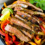 Fajitas de carne servidas sobre una cama de pimientos y cebollas braseados.